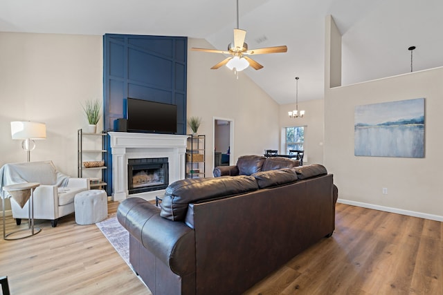 living room with ceiling fan with notable chandelier, a large fireplace, high vaulted ceiling, and light hardwood / wood-style floors