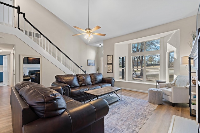 living room with a fireplace, high vaulted ceiling, ceiling fan, and light wood-type flooring