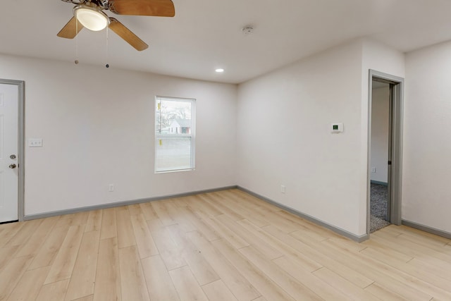 spare room featuring light wood-style flooring, a ceiling fan, and baseboards