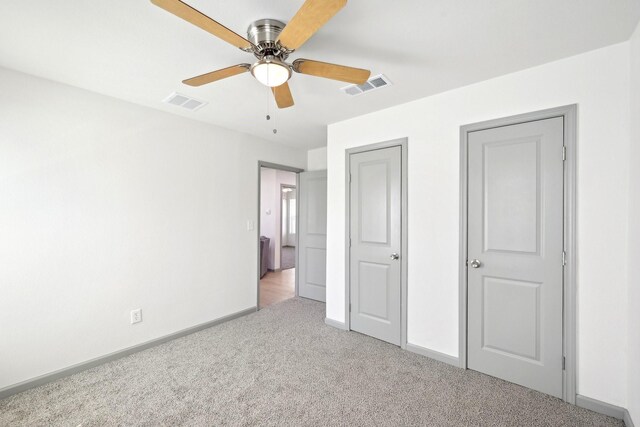 empty room featuring visible vents, light colored carpet, a ceiling fan, and baseboards