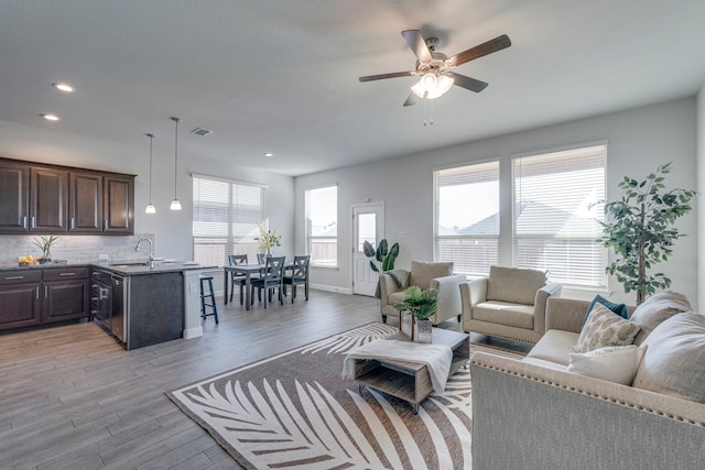 living room with ceiling fan, sink, and light wood-type flooring