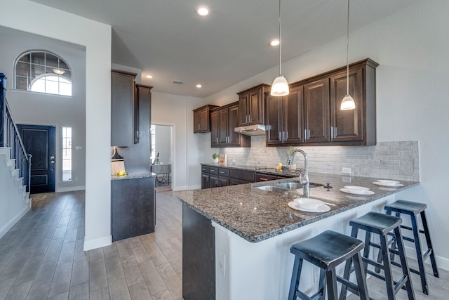 kitchen featuring decorative light fixtures, sink, backsplash, dark stone counters, and kitchen peninsula