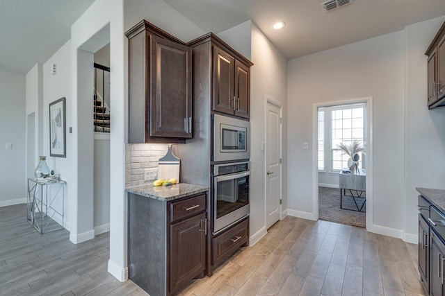 kitchen featuring tasteful backsplash, dark brown cabinets, light wood-type flooring, stainless steel appliances, and light stone countertops