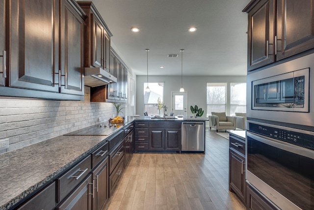 kitchen featuring tasteful backsplash, decorative light fixtures, dark brown cabinets, appliances with stainless steel finishes, and kitchen peninsula