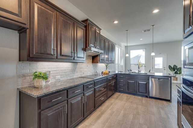 kitchen featuring sink, appliances with stainless steel finishes, decorative backsplash, decorative light fixtures, and dark stone counters