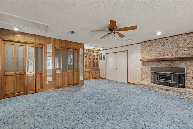 unfurnished living room with ceiling fan, wood walls, a textured ceiling, and carpet flooring