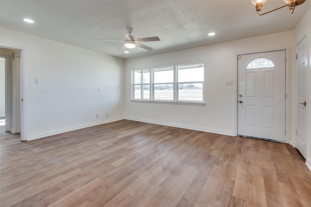 entrance foyer featuring ceiling fan with notable chandelier, light hardwood / wood-style floors, and a textured ceiling