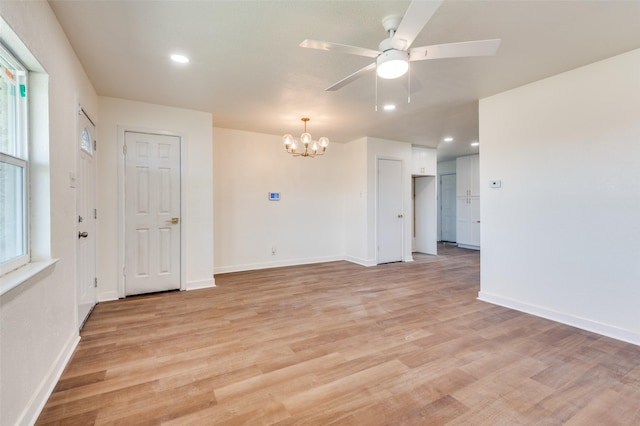 empty room with ceiling fan with notable chandelier and light hardwood / wood-style flooring