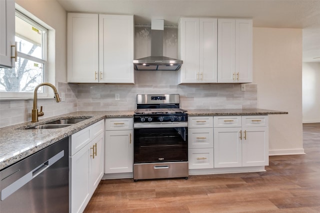 kitchen with stainless steel appliances, sink, wall chimney range hood, and white cabinets