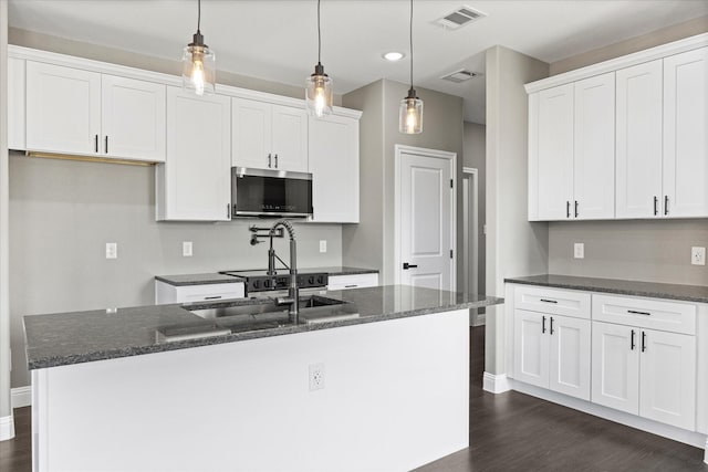 kitchen with an island with sink, dark stone countertops, pendant lighting, and white cabinets