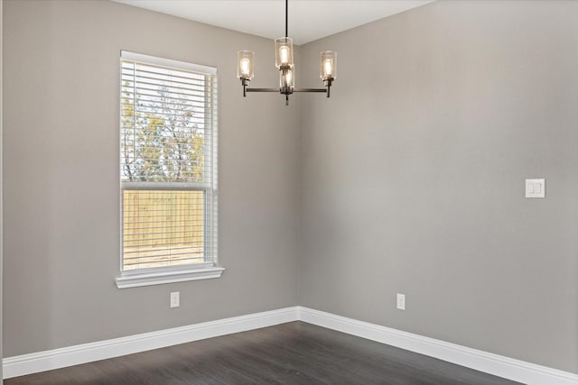 spare room featuring dark wood-type flooring and an inviting chandelier