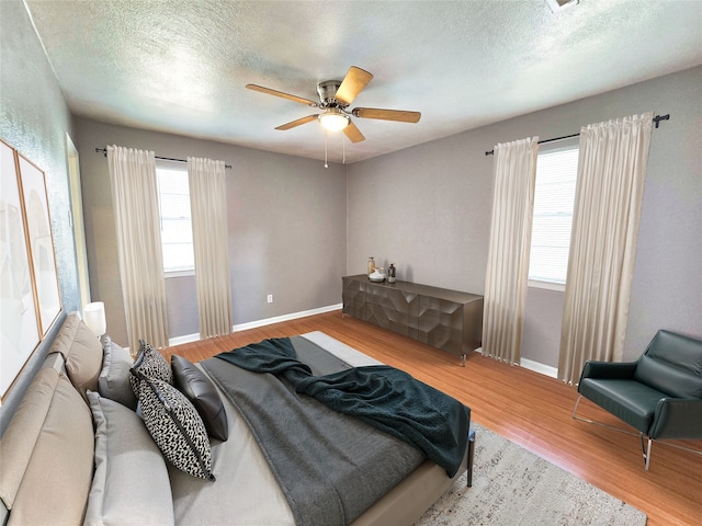 bedroom featuring multiple windows, hardwood / wood-style flooring, a textured ceiling, and ceiling fan