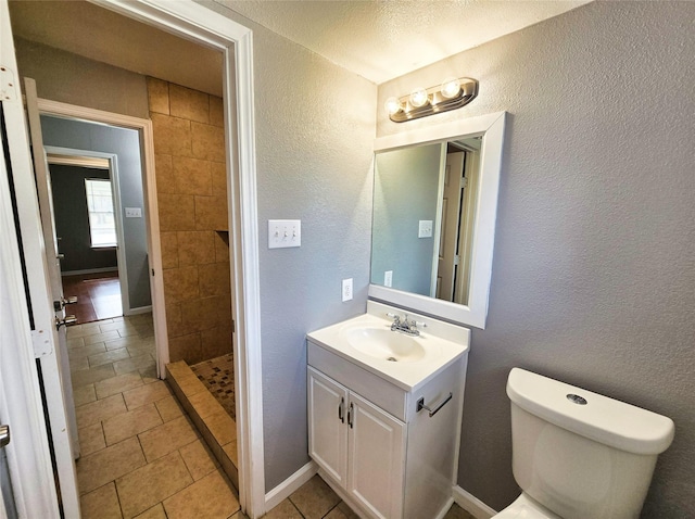 bathroom with tile patterned flooring, vanity, a tile shower, and toilet