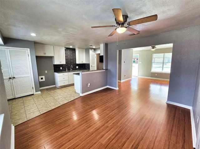 kitchen featuring sink, white cabinetry, a textured ceiling, decorative backsplash, and light wood-type flooring