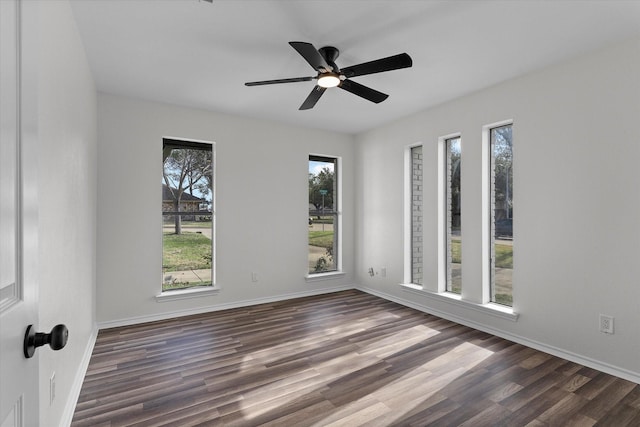 spare room with dark wood-type flooring, a ceiling fan, and baseboards