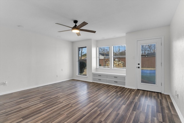 unfurnished living room with a ceiling fan, dark wood finished floors, and baseboards