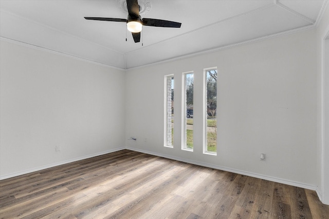 empty room featuring ornamental molding, wood finished floors, a ceiling fan, and baseboards