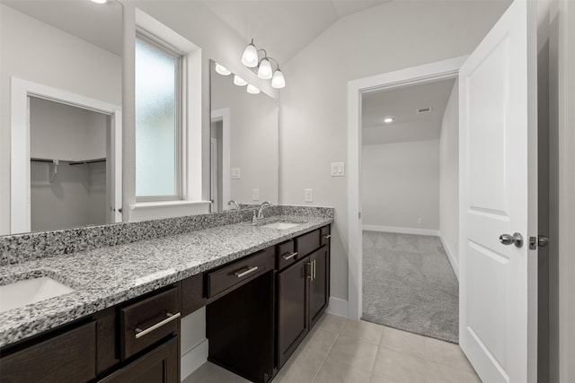 full bath featuring a walk in closet, double vanity, lofted ceiling, a sink, and tile patterned flooring