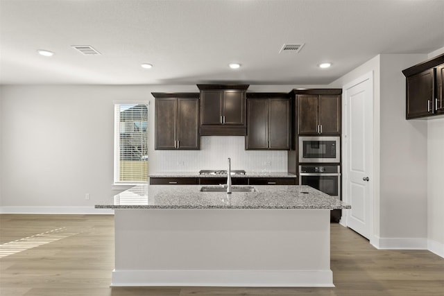 kitchen featuring stainless steel appliances, tasteful backsplash, visible vents, dark brown cabinetry, and light stone countertops