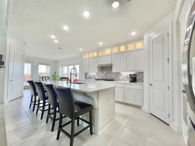 kitchen with sink, a kitchen island with sink, white cabinetry, a kitchen bar, and decorative backsplash