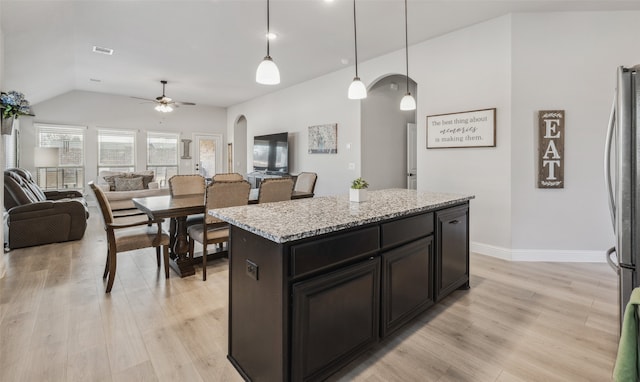 kitchen featuring arched walkways, pendant lighting, a kitchen island, and light wood-style floors