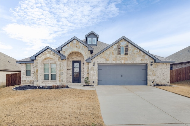 french country home with driveway, stone siding, a garage, and fence