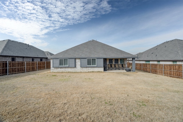 rear view of property featuring a shingled roof, a fenced backyard, a patio, and a lawn