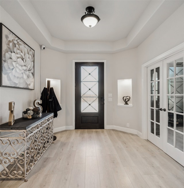 foyer entrance with wood finished floors, french doors, a raised ceiling, and baseboards