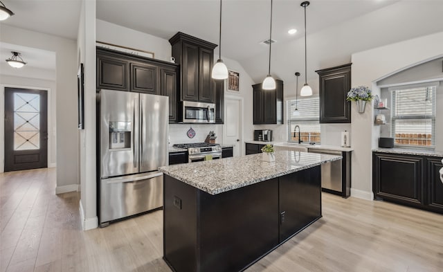 kitchen featuring light wood-style flooring, a kitchen island, a sink, appliances with stainless steel finishes, and tasteful backsplash