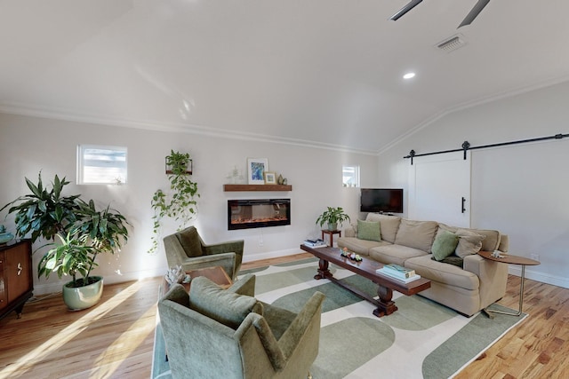 living room with ornamental molding, a barn door, vaulted ceiling, and light wood-type flooring