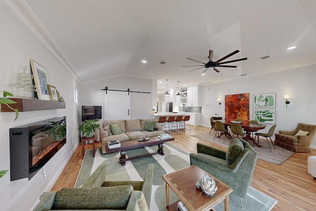 living room featuring crown molding, a barn door, light hardwood / wood-style floors, and vaulted ceiling