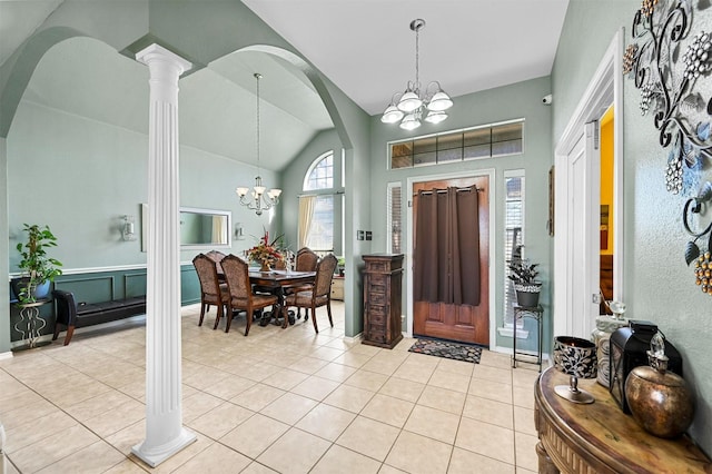 foyer entrance with decorative columns, vaulted ceiling, light tile patterned floors, and a chandelier