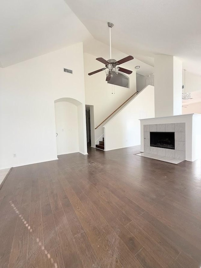 unfurnished living room with dark wood-type flooring, ceiling fan, a tiled fireplace, and high vaulted ceiling