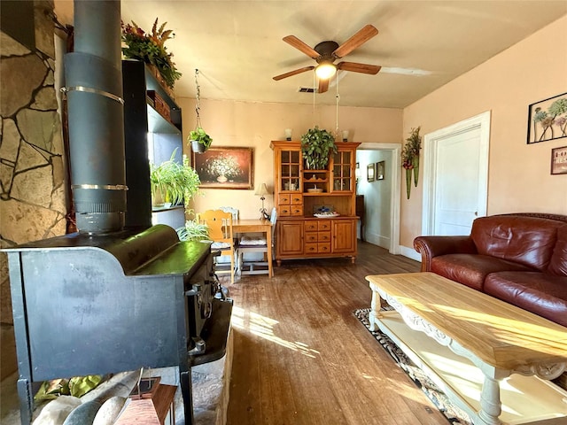 living area with a wood stove, dark wood-style floors, visible vents, and a ceiling fan