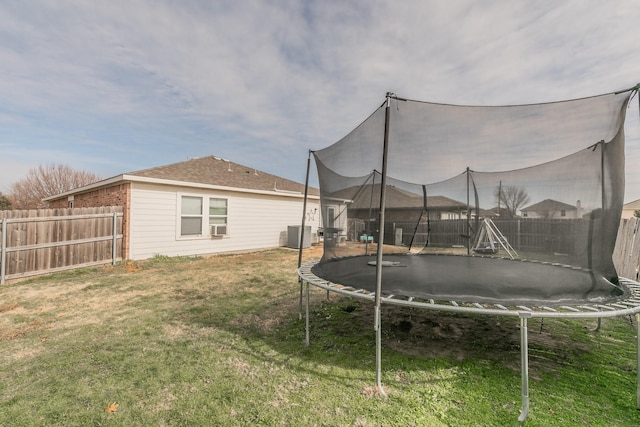 rear view of property with central AC unit, a trampoline, and a lawn