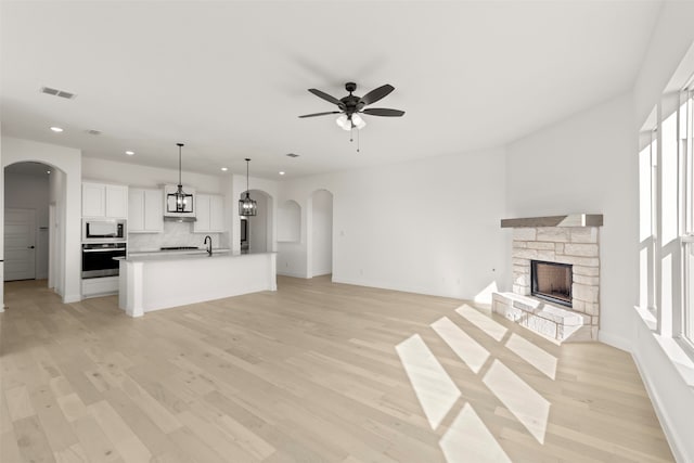 unfurnished living room with light hardwood / wood-style flooring, sink, a fireplace, and ceiling fan