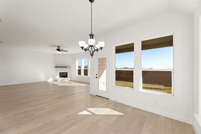 unfurnished living room with ceiling fan with notable chandelier, a fireplace, and light hardwood / wood-style floors