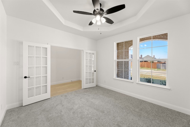 carpeted empty room with french doors, ceiling fan, and a tray ceiling