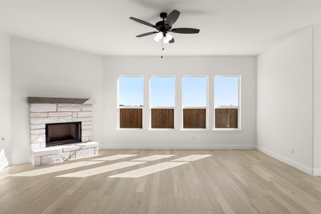 unfurnished living room featuring ceiling fan, a stone fireplace, a healthy amount of sunlight, and light wood-type flooring