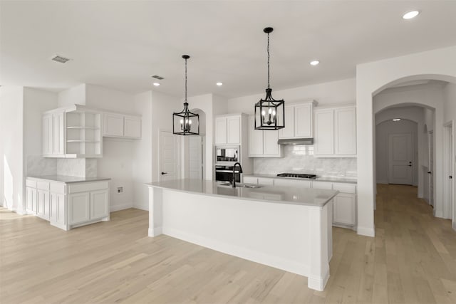 kitchen with backsplash, appliances with stainless steel finishes, white cabinets, and a center island with sink