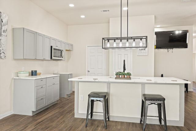 kitchen with gray cabinets, a kitchen island with sink, a breakfast bar area, and decorative light fixtures