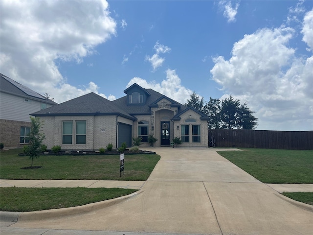 french country style house with brick siding, fence, a front lawn, concrete driveway, and an attached garage