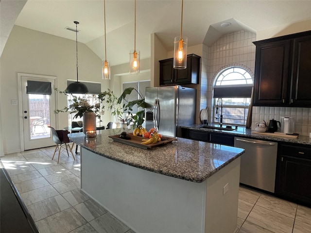 kitchen featuring appliances with stainless steel finishes, sink, backsplash, dark stone counters, and a center island