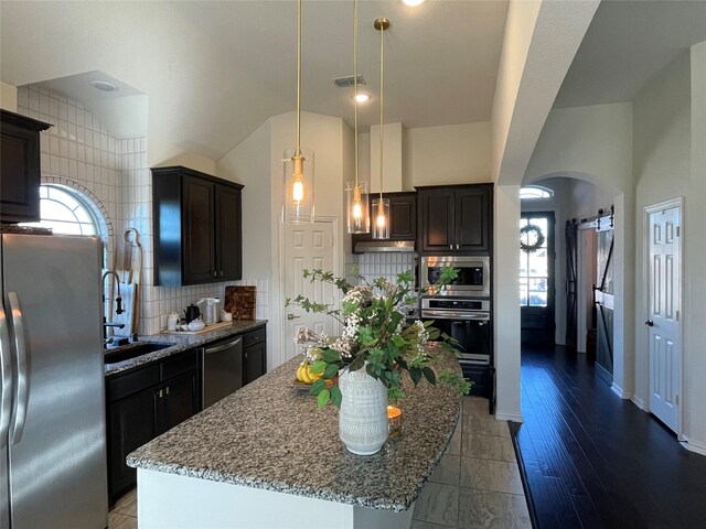 kitchen with light stone counters, a sink, arched walkways, stainless steel appliances, and backsplash