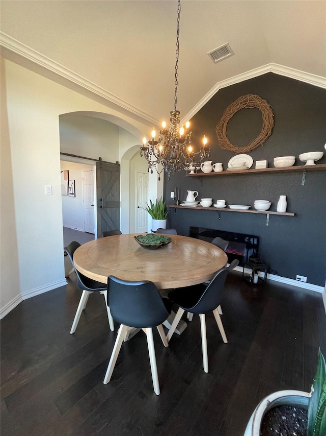 dining space with vaulted ceiling, ornamental molding, a barn door, and wood-type flooring