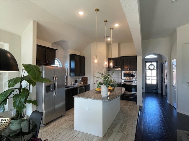 kitchen with backsplash, hanging light fixtures, stainless steel appliances, dark brown cabinetry, and a kitchen island