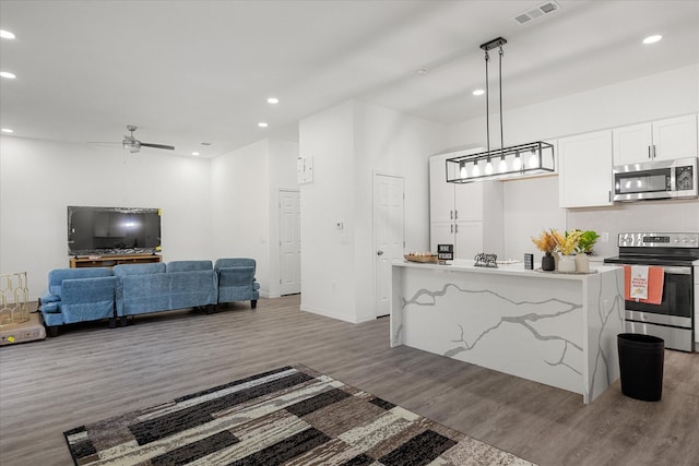 kitchen with a kitchen island, white cabinets, hanging light fixtures, stainless steel appliances, and dark wood-type flooring