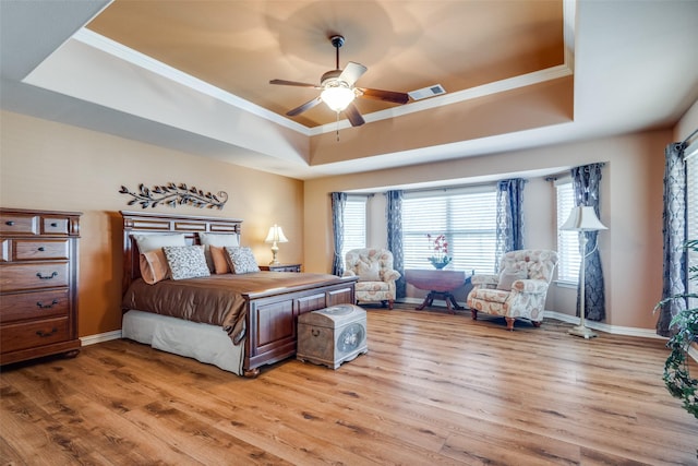 bedroom with ceiling fan, ornamental molding, a raised ceiling, and light wood-type flooring