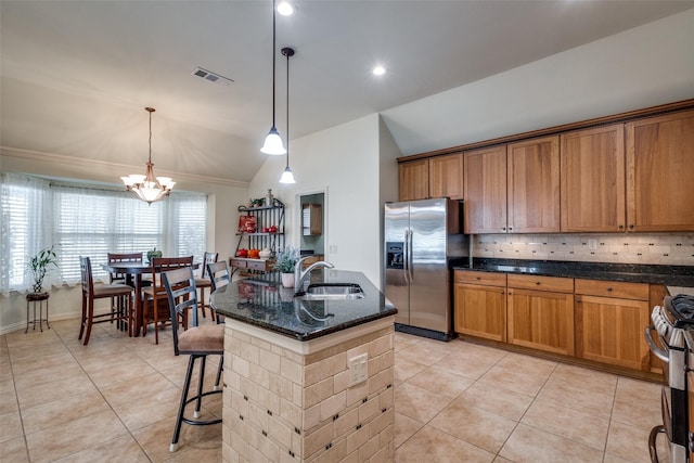 kitchen with appliances with stainless steel finishes, lofted ceiling, sink, hanging light fixtures, and a kitchen island with sink