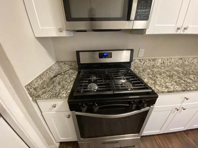 kitchen with dark wood-type flooring, appliances with stainless steel finishes, light stone countertops, and white cabinets